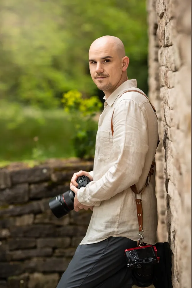 Portrait eines Fotografen mit Kamera an einer Natursteinmauer